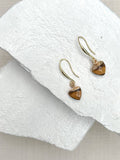Tiger's eye heart drop earrings on gold plated hooks resting on white stone