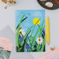 Onneke Travel Logbook with an illustrated meadow cover featuring white daisies, purple wildflowers, tall green grass, a yellow sun and birds in flight against a blue sky.