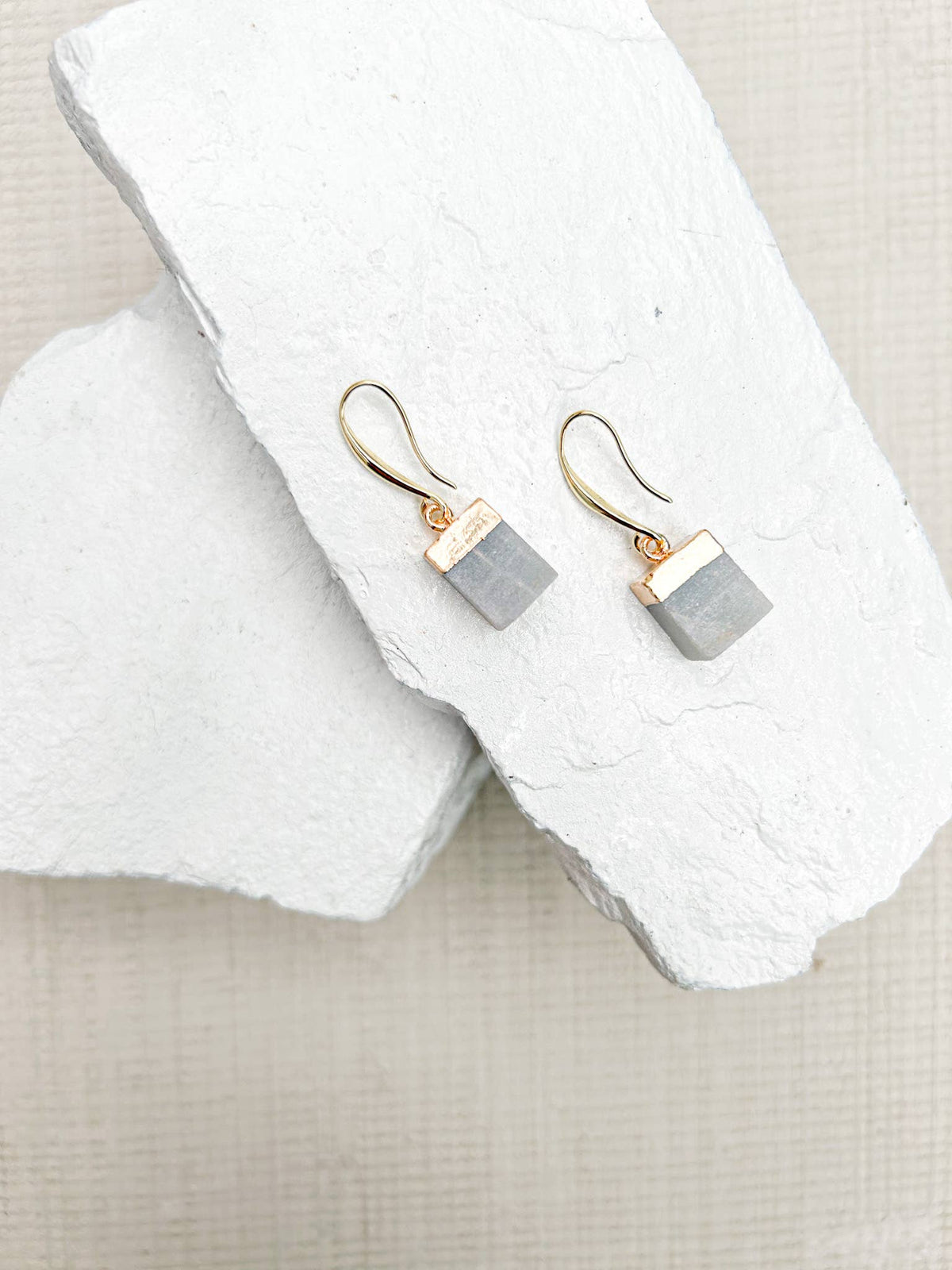 
Pair of gold hook earrings with blue-grey amazonite cube drops on a white textured stone display