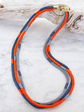 Long three strand cord necklace in orange, navy and grey with gold tone clasp and extender chain