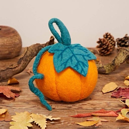 Handcrafted orange felt pumpkin with teal felt leaf and curling vine surrounded by autumn leaves