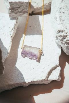 Natural amethyst slice pendant necklace on gold chain resting on white stone