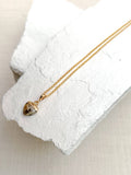 Dalmatian jasper heart pendant necklace on fine gold plated chain resting on white stone
