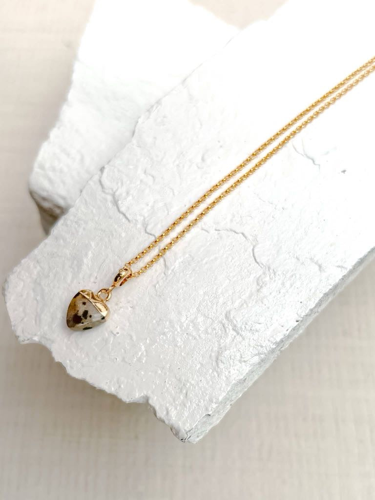 Dalmatian jasper heart pendant necklace on fine gold plated chain resting on white stone