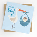 Square new baby boy greeting card with a soft blue background featuring a collage-style illustration of a stork carrying a baby boy in a blue bundle, with teal script reading "it's a boy," shown alongside a kraft brown envelope.