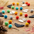 Felt Halloween garland with colourful pom poms, white ghosts and black bats on a wooden table
