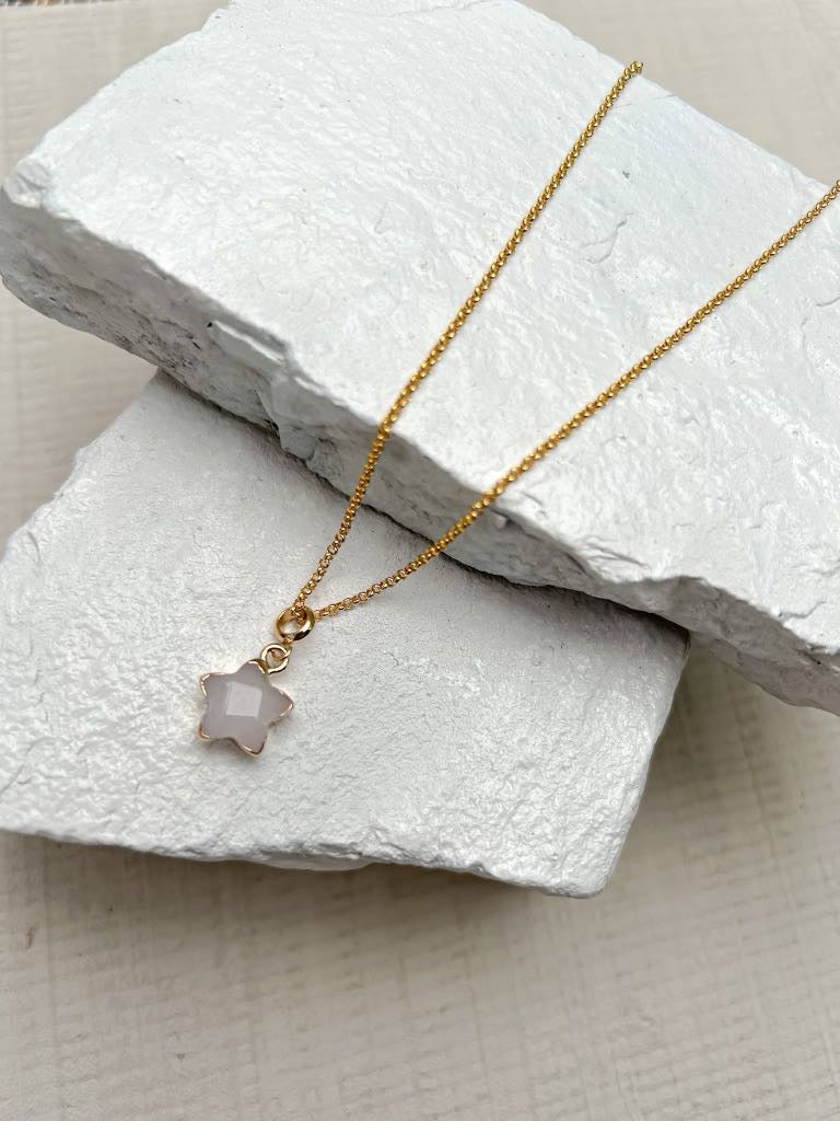 White jade star pendant necklace on fine gold plated chain resting on white stone