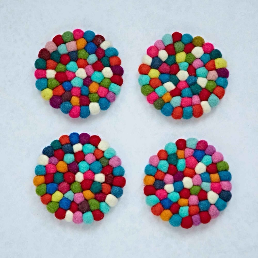 Set of four multicolour felt ball coasters, with one holding a glass of water on a wooden table