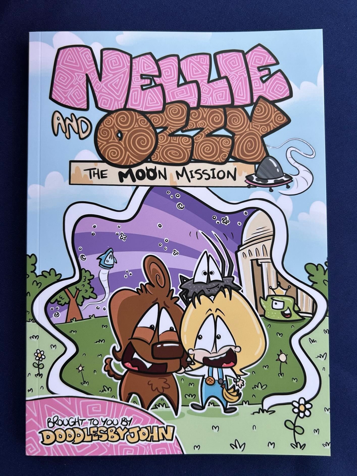 Nellie and Ozzy The Moon Mission, a colourful comic-style illustrated children's book written and illustrated by local Belfast artist DoodlesByJohn, featuring cartoon characters Nellie and Ozzy on a moon mission adventure with bright, bold artwork.