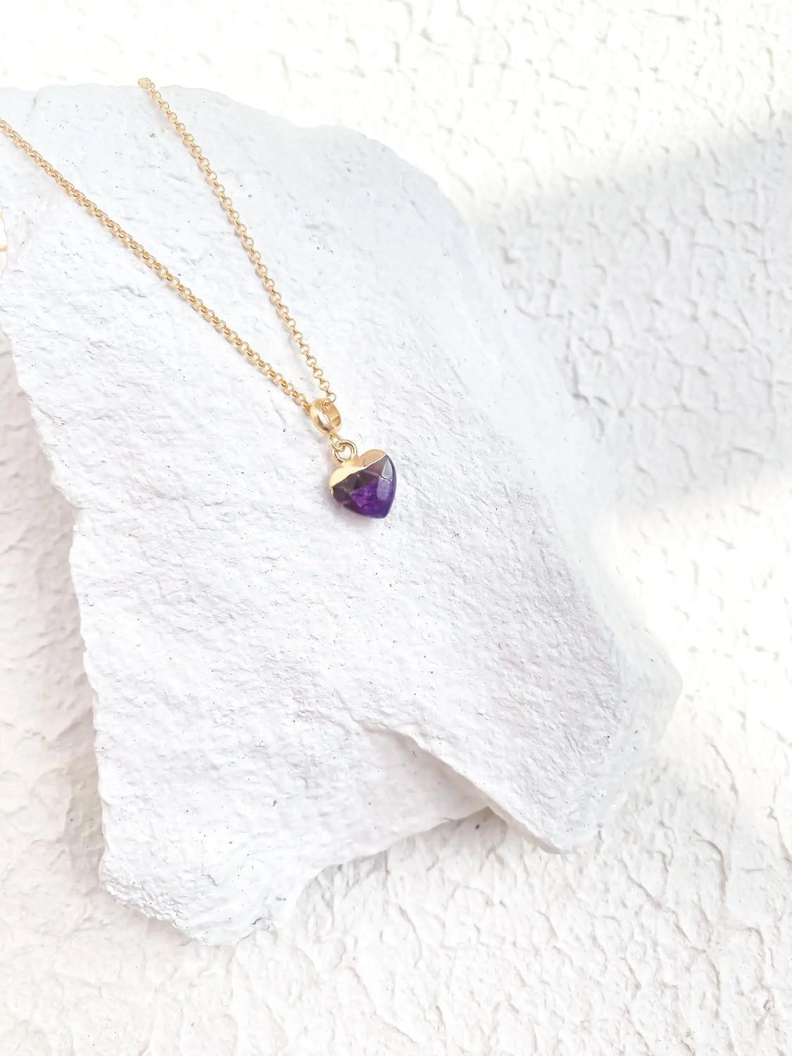  Amethyst heart pendant necklace on fine gold plated chain resting on white stone