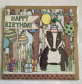 A hand-illustrated birthday card featuring a badger with a party hat, balloons, and gifts in a forest setting. The card has a kraft brown envelope and is blank inside for a personal message.