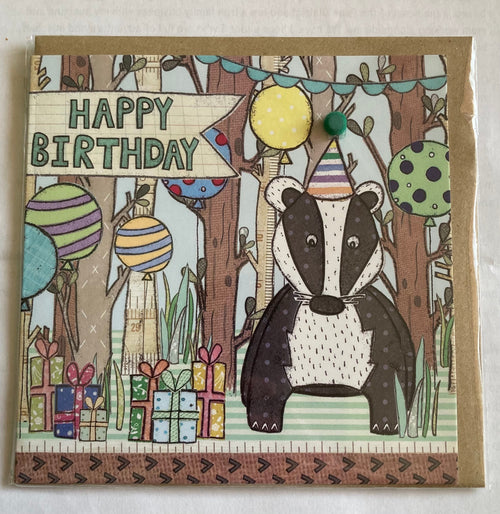 A hand-illustrated birthday card featuring a badger with a party hat, balloons, and gifts in a forest setting. The card has a kraft brown envelope and is blank inside for a personal message.